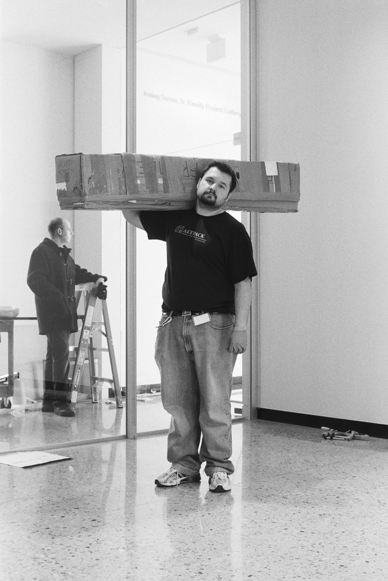 Walead Besht photograph portrait of a man wearing jeans and black t-shirt carrying a large package over his shoulder