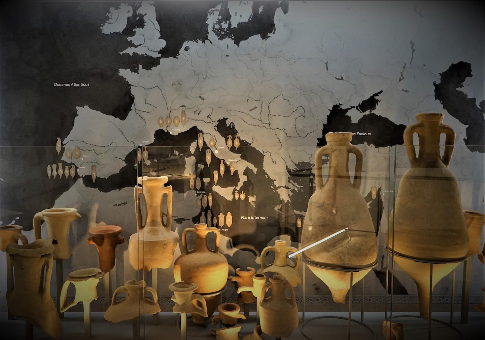 Arrangement of amphorae from across the Mediterranean. Backed by a map with info on the orgins of these vessels.