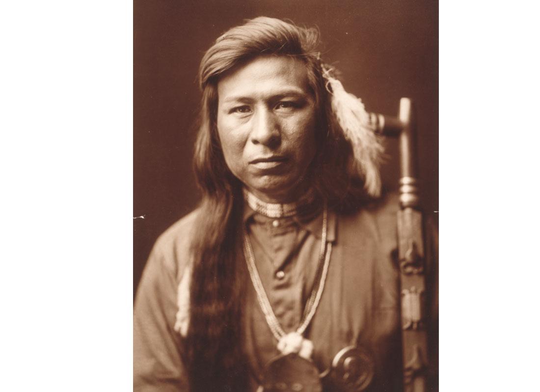Tah It Way, head-and-shoulders portrait, facing front, peace pipe on right, 1905.